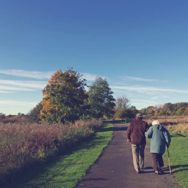 A happy older couple strolling hand-in-hand on a sandy beach as the sun sets, casting a warm glow over the scene.